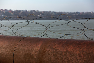 Old rusty barbed wire fence on a large rusty overpass pipe. Territory Security Wire Fence