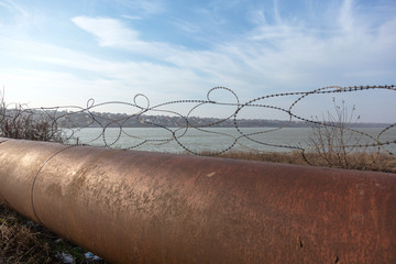 Old rusty barbed wire fence on a large rusty overpass pipe. Territory Security Wire Fence