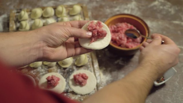 Rows of prepared dumplings lie on wooden board. Process of cooking Russian dumplings. Man hands is making pelmeni. Dumplings stuffed with minced meat. Manually sculpts dumplings. Rustic style backdrop