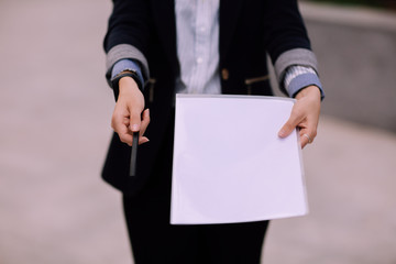 Young successful business woman in jacket holds out black pencil and folder with white sheets of paper
