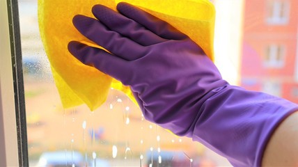 hand in a rubber glove with a napkin washes a window in a house