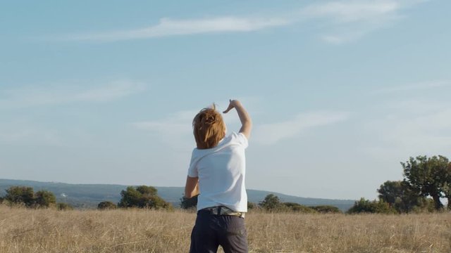 Back view of young boy flying paper airplane in summer field