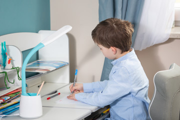 Naklejka na ściany i meble learn form home - lovely small boy in blue shirt writing at the desk