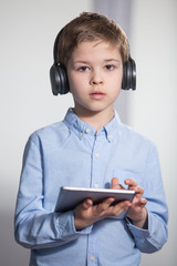 technology - a lovely young pupil standing with his tablet wearing headphones