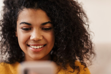 Image of joyful african american woman using cellphone and smiling