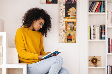 Image of serious african american woman reading book while sitting