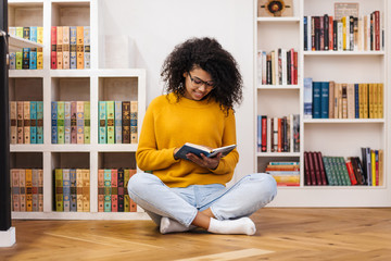 Image of joyful african american woman reading book while sitting