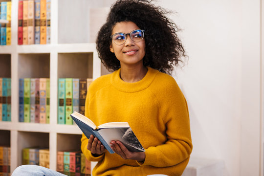 Image of joyful african american woman reading book while sitting