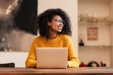 Image of cheerful african american woman in eyeglasses using laptop