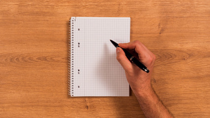 Notizblock auf Holzschreibtisch mit Hand und Stift