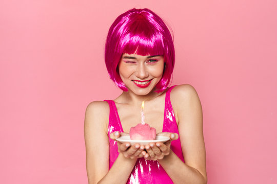 Image of excited cute woman winking and holding cake with candle