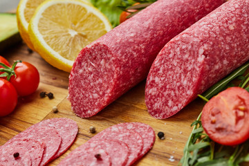 Traditional thinly sliced salami on a wooden cuttingboard  with spices, lettuce, avocado and tomatoes. Cold meat plate