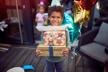 young little boy carrying birthday presents looking at camera. Birthday celebration. Eye contact