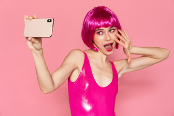 Image of young girl wearing wig smiling and taking selfie on cellphone