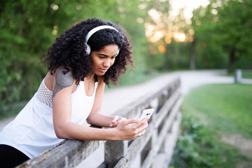 Lachende junge Frau beim Sport, sie trägt Kopfhörer und hat ihr Handy in der Hand 