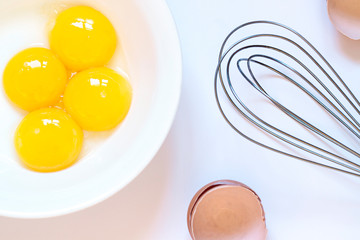 Fresh raw chicken yolks with whisk, eggs shells on the white background. Baking or food preparation concept close up. 