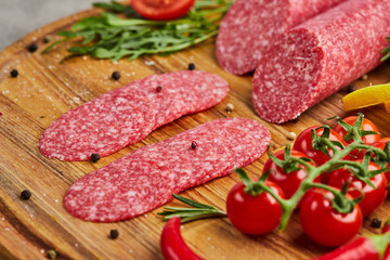 Traditional thinly sliced salami on a wooden cuttingboard  with spices, lettuce, avocado and tomatoes. Cold meat plate