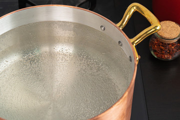 Copper pot with boiling water on a gas stove close up