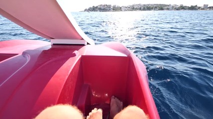 Male, men twists her feet on pedals of catamaran swimming sport facility for relaxing walks on sea water. Male hairy bare legs pedal on double plastic catamaran. Catamaran swims towards shore.
