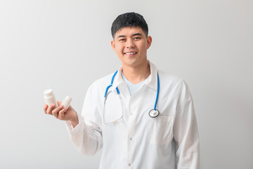 Male Asian doctor with pills on light background