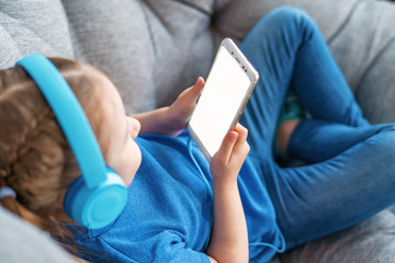 little girl with headphones and holding smartphone white screen in her hands