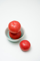 Tomatoes in a blue porcelain bowl.Tomato on white background. Three tomatoes placed on a white desktop.