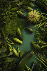 Świeże zielone surowe warzywa i zioła - cukinia fasolka szparagowa ogórek dynia pietruszka koperek lubczyk na ciemnym i nastrojowym zielonym jednolitym tle