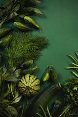 Świeże zielone surowe warzywa i zioła - cukinia fasolka szparagowa ogórek dynia pietruszka koperek lubczyk na ciemnym i nastrojowym zielonym jednolitym tle - obrazy, fototapety, plakaty
