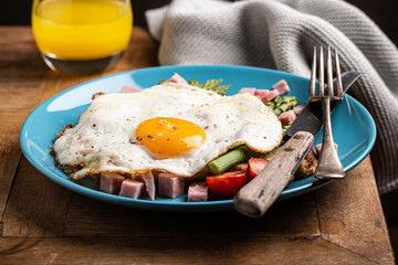 Healthy breakfast or lunch with fried egg, bread toast, green asparagus and tomatoes on blue plate on old wooden table