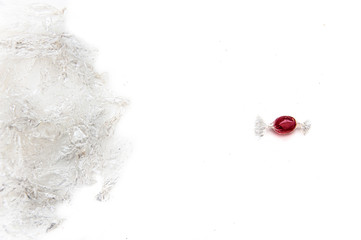 One is a red candy in front of a bunch of candy wrappers. White background. Nutrition concept. Relashionship concept. Copyspace