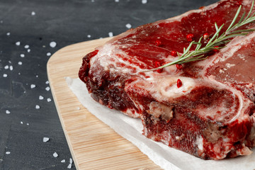 Raw fresh meat t-bone steak with spices on a dark background, close up
