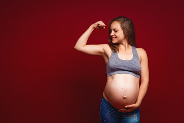 Slender pregnant girl in sportswear demonstrates bicep of arm muscle