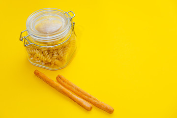 The closed bank with italian pasta and the snacks are  around it  on yellow background. Food delivery, coronavirus, crisis concept. Flat lay and place for text.