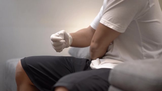 4k Asian man put on white protective gloves sitting on gray couch background, self home quarantine, stop illness from spreading, germ virus prevention, Corona virus 2019, COVID 19, healthcare medical