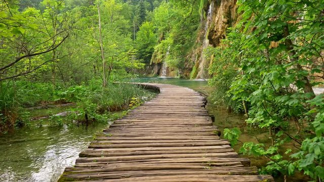 Walking the wooden boardwalk among lakes and waterfalls and rich green flora in Plitvice Lakes National Park, Croatia. Steadicam shot, 4K