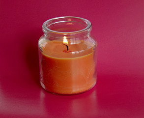 a fragrant pink candle in a decorative jar flickers with its fire.