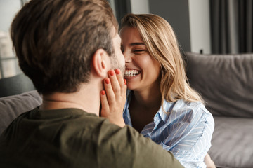 Photo of cheerful couple laughing and hugging while sitting on sofa