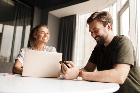 Photo of joyful couple using laptop and mobile phone while sitting