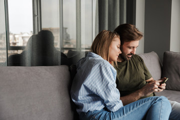 Photo of pleased beautiful couple hugging and using mobile phone