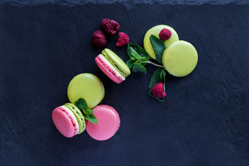 Sweet colorful French macaroons cookies dessert on black wooden background.The composition is decorated with raspberries, mint leaves.copy space.Concept of tasty confectionery food.