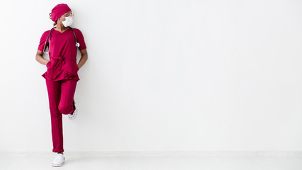 Long view of black woman medic leaning on white wall