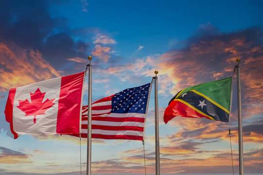 Flags of St Kitts United States and Canada flying under blue sky