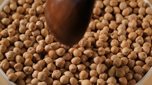 Dry uncooked chickpea falling from spoon into white bowl. Food video macro