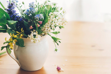 Wildflowers bouquet in old cup on wooden table,  space for text. Blooming spring flowers in soft light, rural still life. Happy  Mother's day. Hello spring.