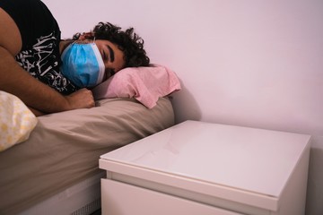 A man sleeping on his bed wearing a surgical mask on the new normal life after covid 19 coronavirus global pandemic and sanitary crisis