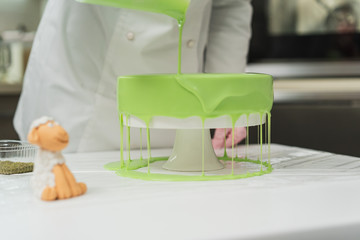 Pastry cook prepares a cake of green, watering it with icing