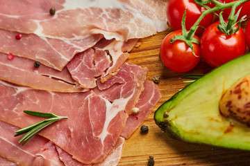 Italian prosciutto crudo or spanish jamon. Raw ham on stone cutting board decoreted with spices, lettuce, lemon, tomatoes and avocado