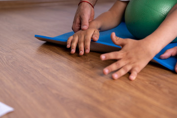 Little boy with cerebral palsy has musculoskeletal therapy by doing exercises on floor mat. Child give hand therapist - obrazy, fototapety, plakaty