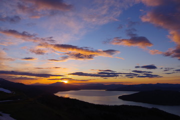 Fototapeta na wymiar 峰から望む夜明けの空のグラデーション。朝の太陽に照らされた雲。眼下の湖。北海道、日本。