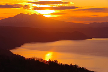 湖を照らす夜明けの太陽。美しい稜線のシルエット。朝焼けの空に浮かぶ雲。美幌峠からの朝の眺め。北海道、日本。